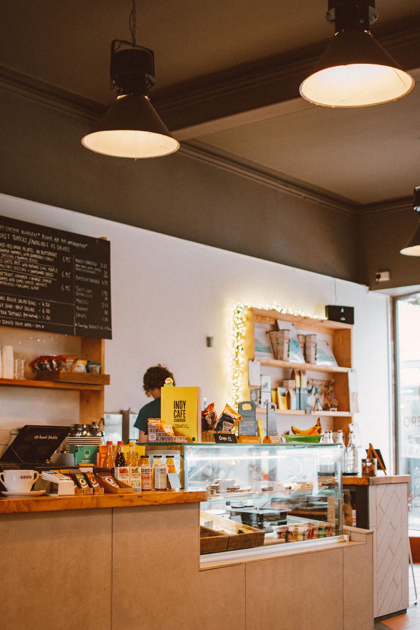 A welcoming café counter with a point of sale terminal, food display and barista.