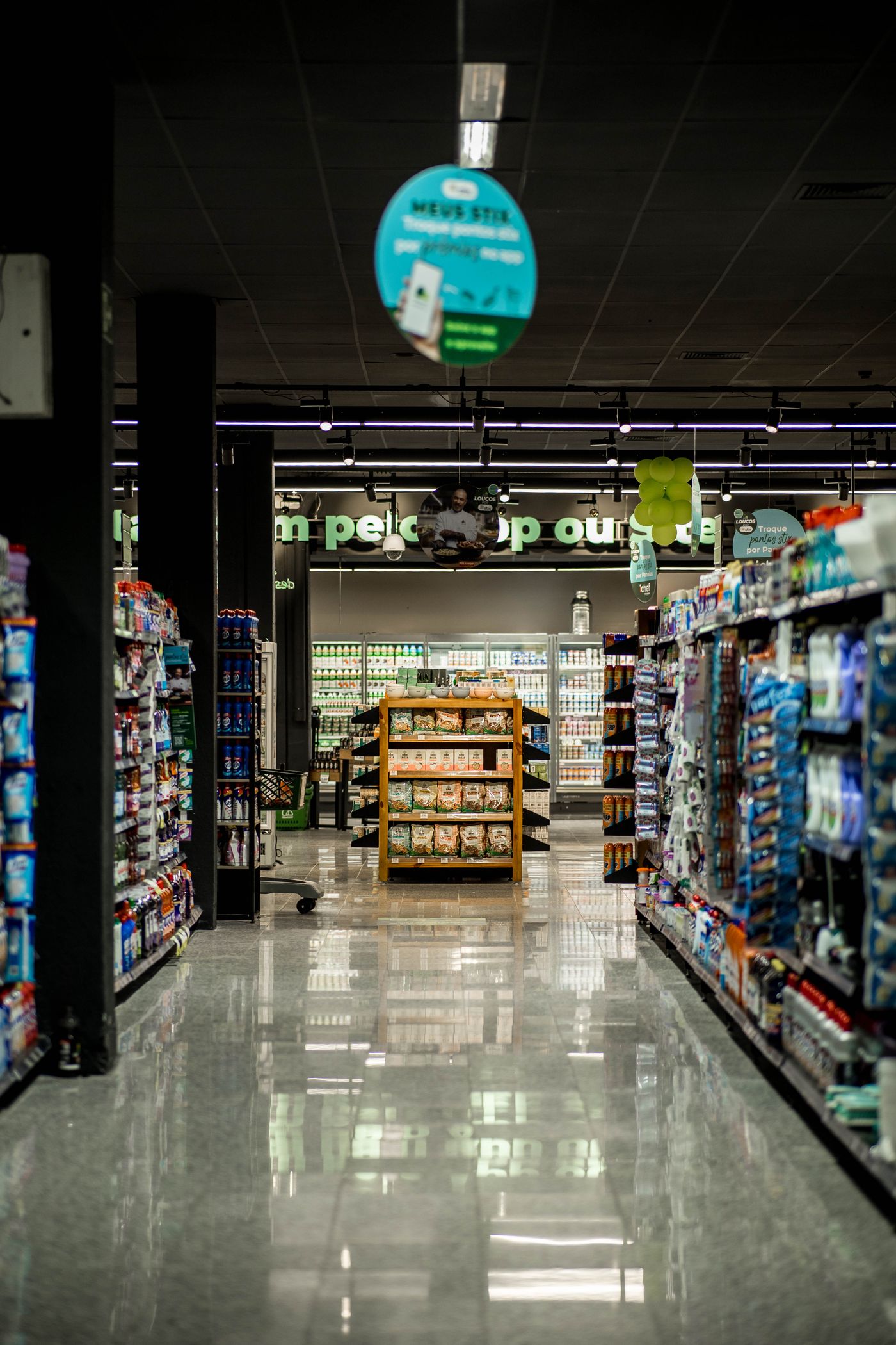 An organised supermarket aisle with stocked grocery shelves and a central product display.