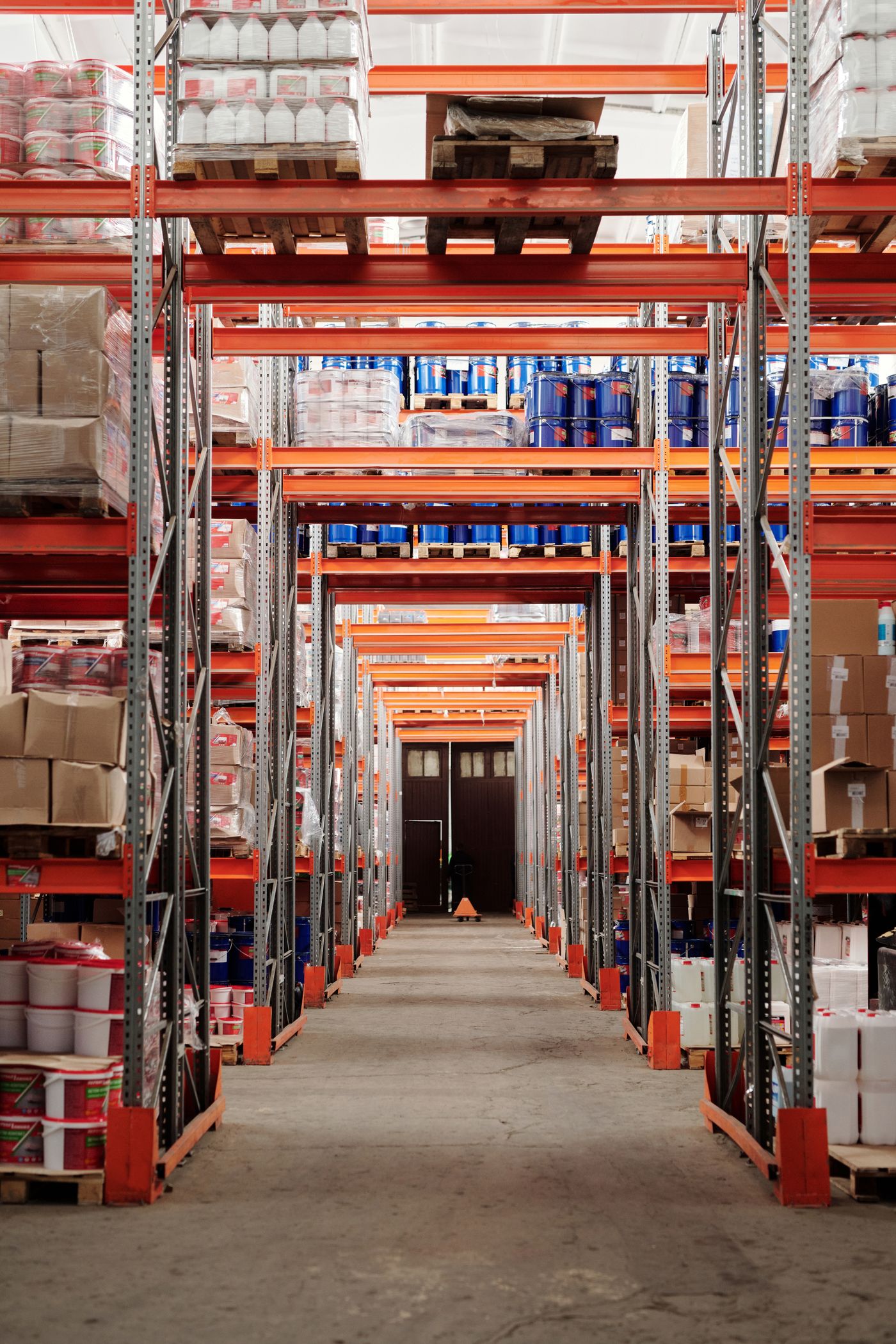An industrial warehouse with tall orange shelving, labelled goods and a clear dispatch aisle.